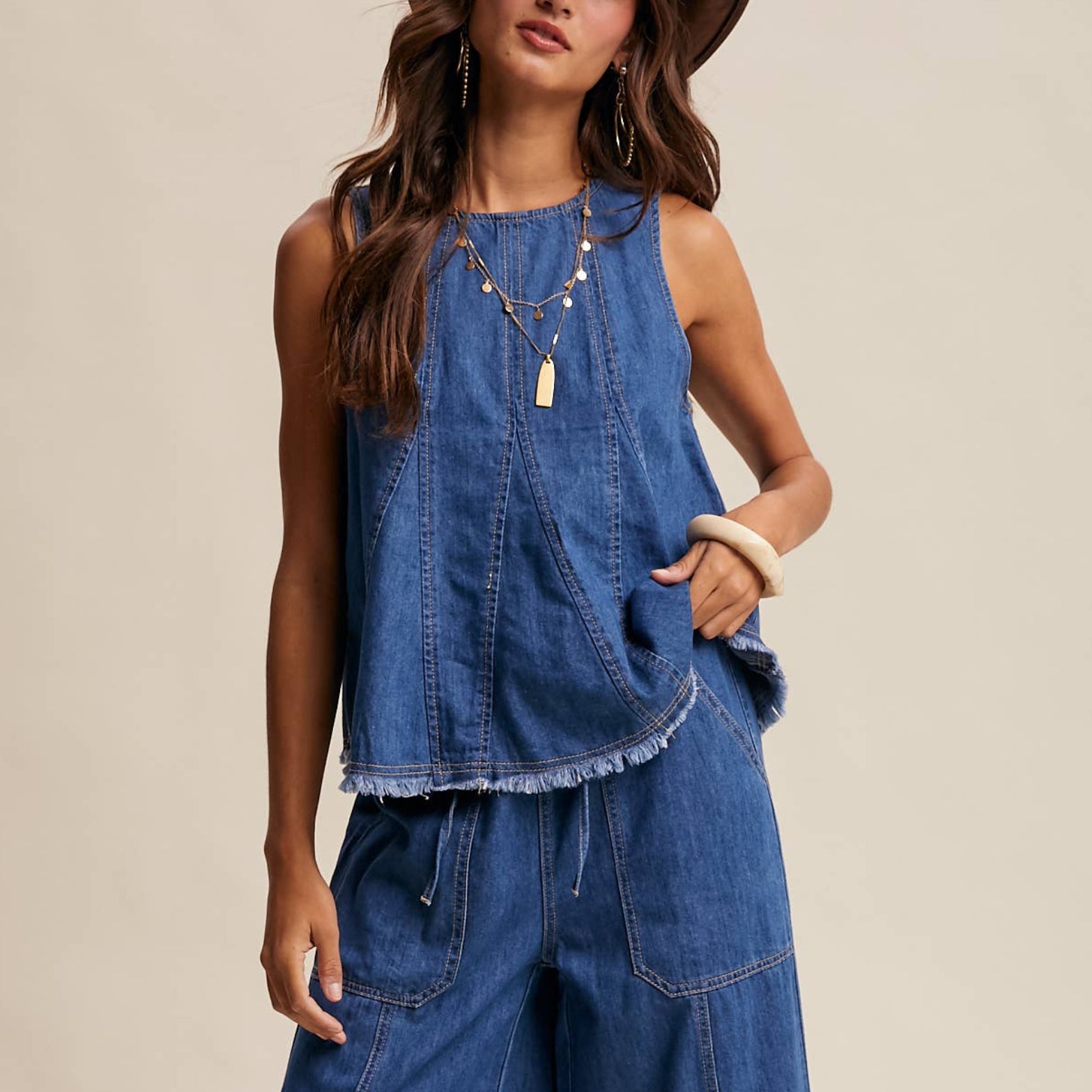 Woman wearing a blue denim outfit with a brown hat on a beige background